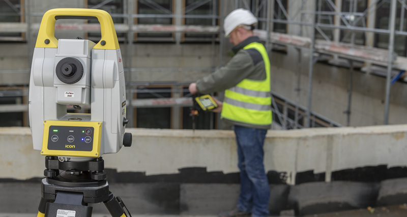 Leica iCT30墨出しツールで、コンクリート平板上に短い建設用プリズムポールを設定する、黄色いベストを着用した建設作業員。